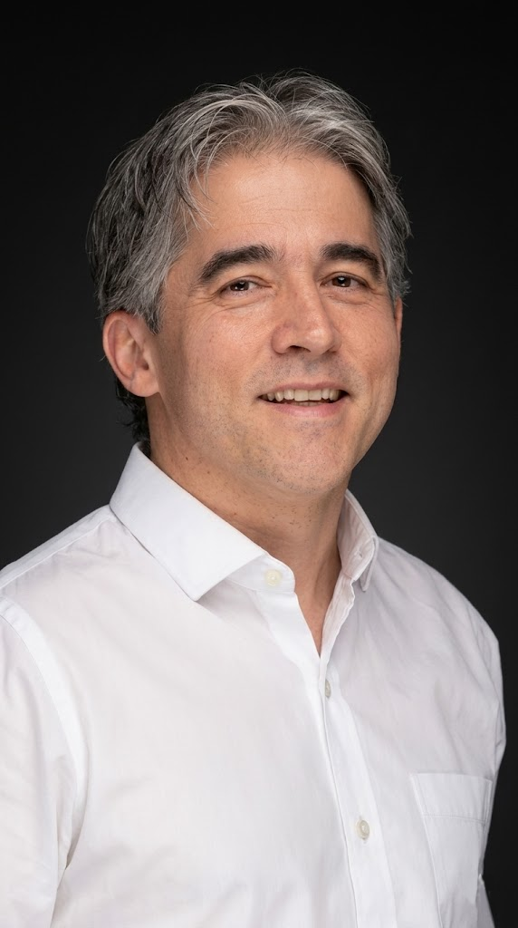 Smiling man with salt-and-pepper hair wearing a white button-down shirt